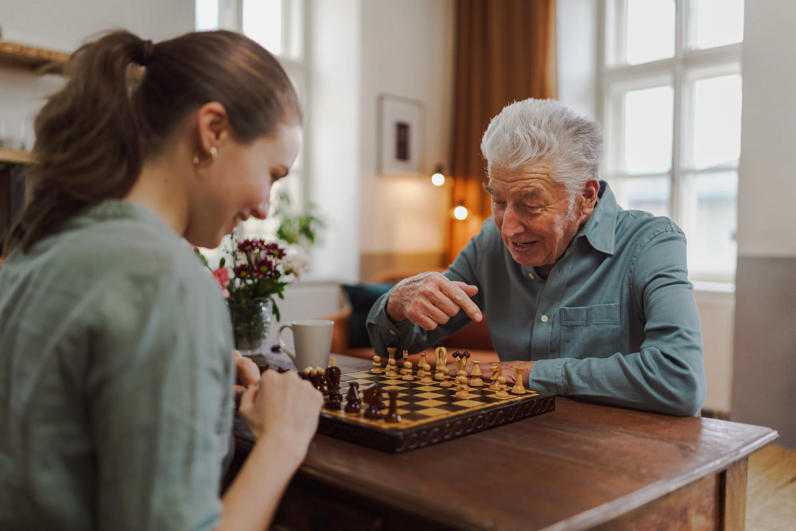 Senior beim Schachspiel mit einer Pflegekraft am Tisch