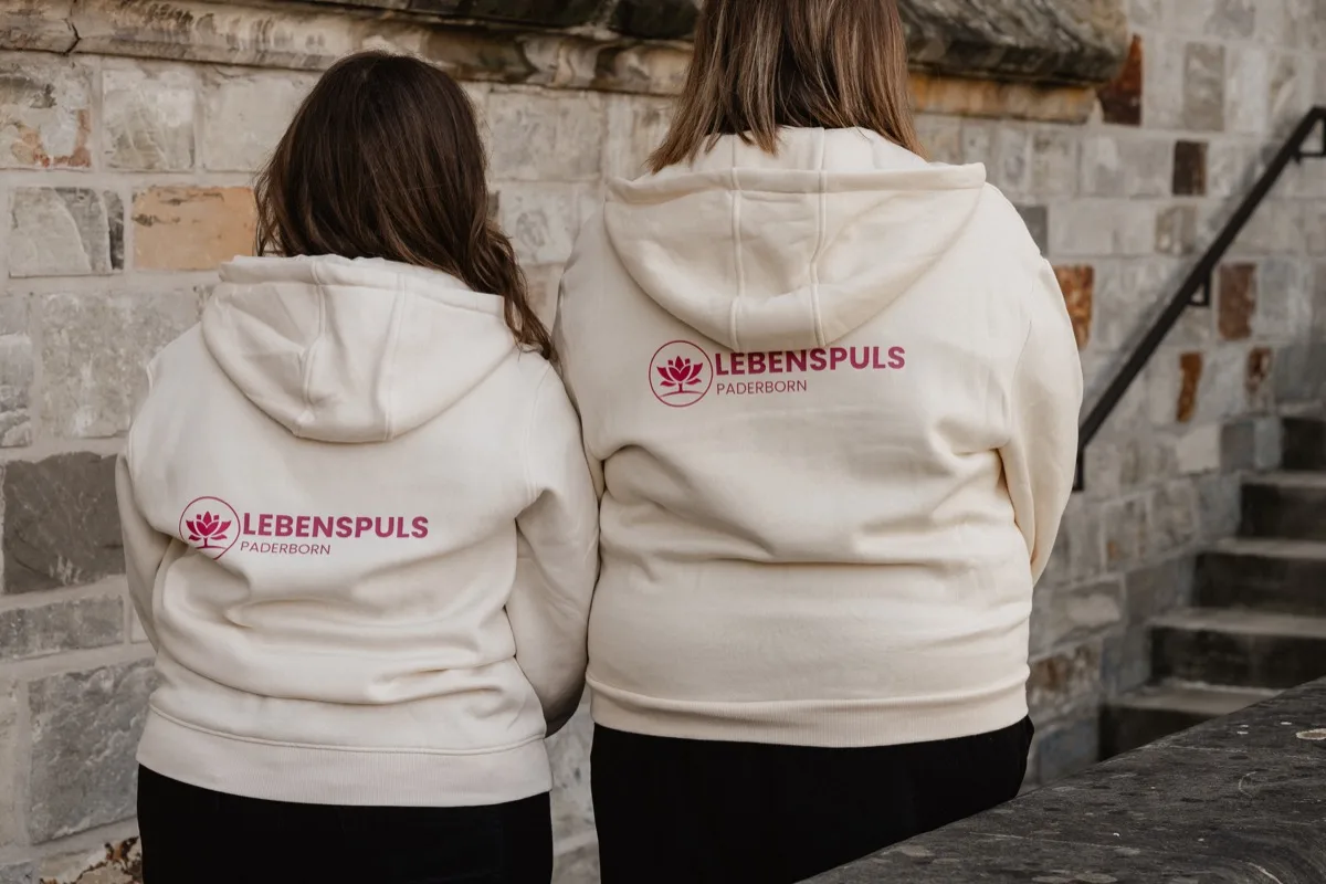 Zwei Mitarbeiterinnen von Lebenspuls von hinten im Lebenspuls-Hoodie