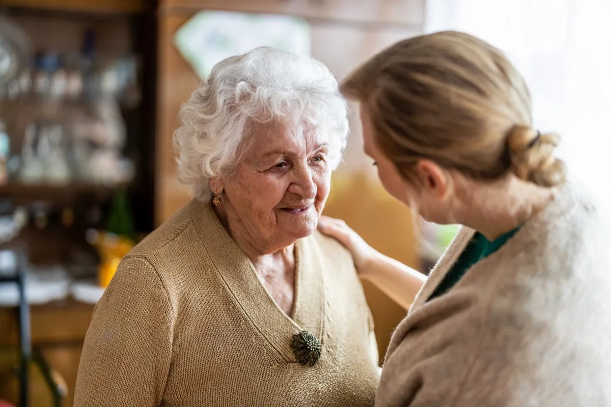 Pflegekraft im Gespräch mit einer Seniorin im Wohnzimmer