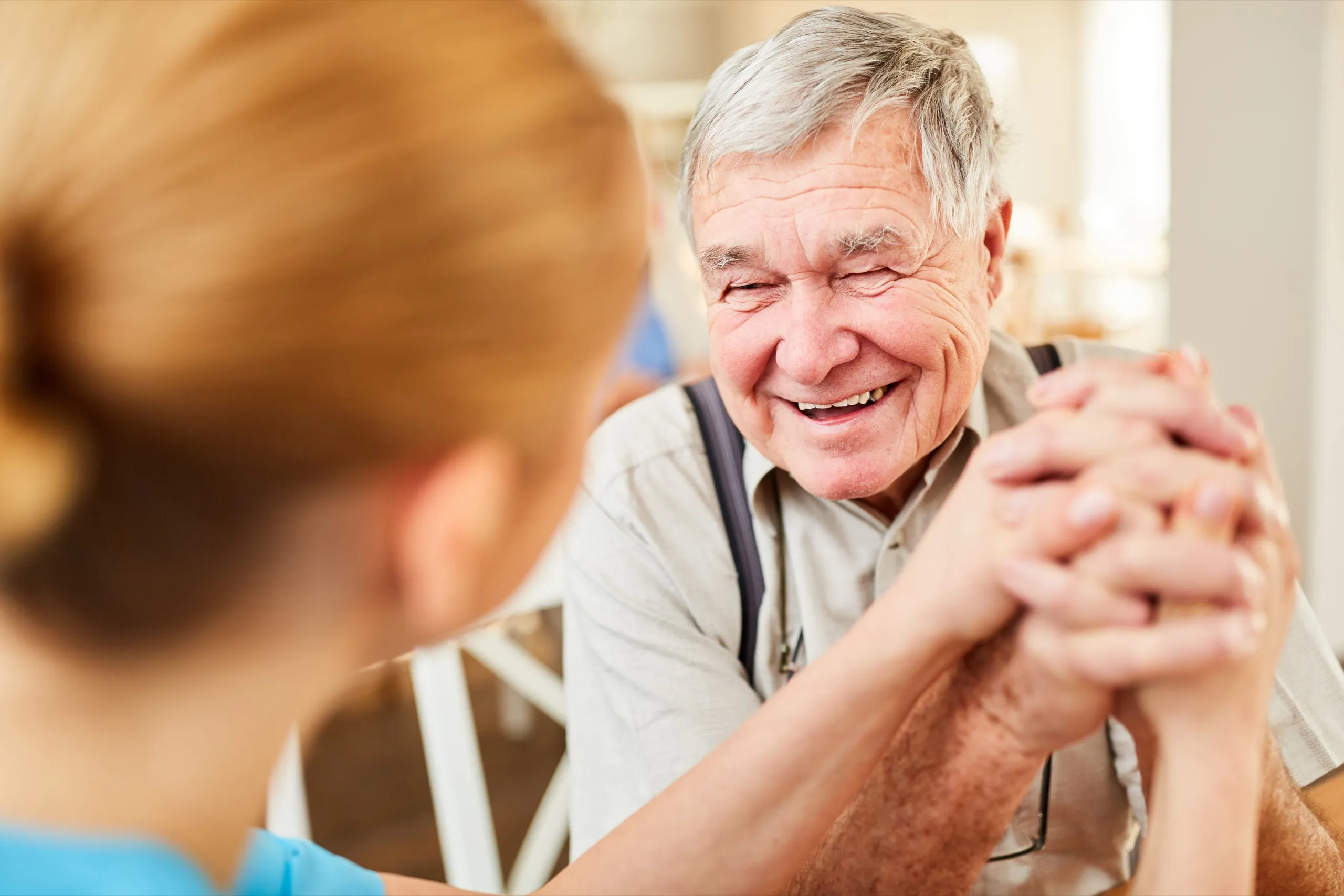 Pflegekraft hält die Hand eines lachenden Seniors